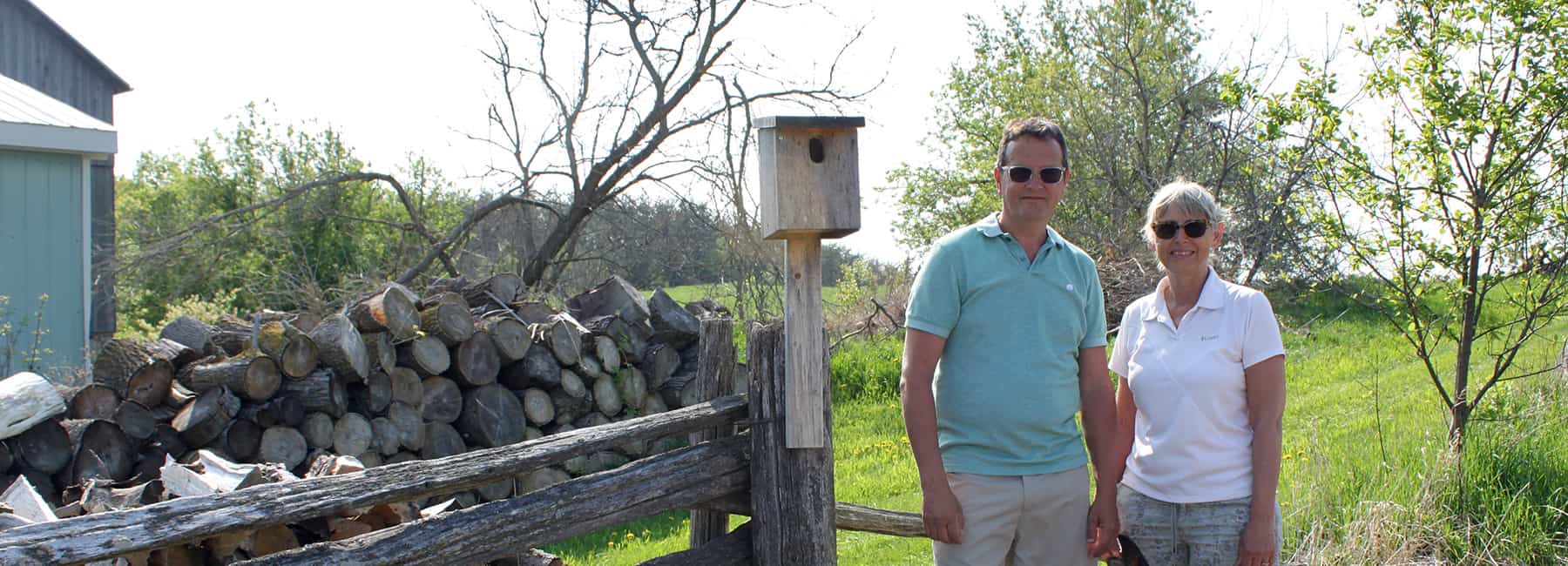 Two landowners standing outdoors beside a bird box installed on a fence on their rural property.